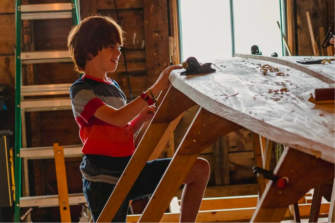 A child working on a wooden boat in the Islesford Boatworks shop
